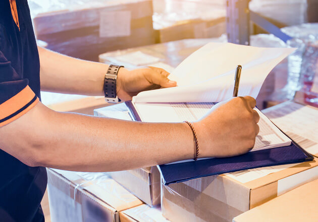 Close up of hand signing documentation on stack of packages