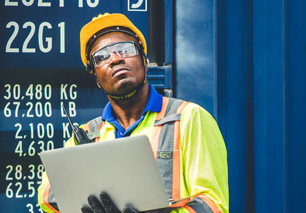 Man in hardhat and safety jacket holding a laptop and looking up