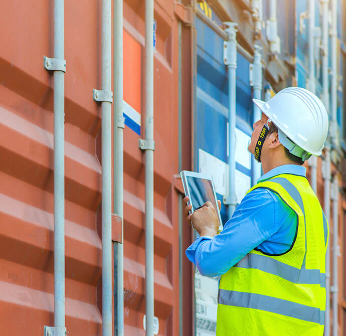 Man in hardhat and safety vest inspecting containers